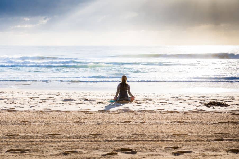 A woman sits and meditates on a beach
