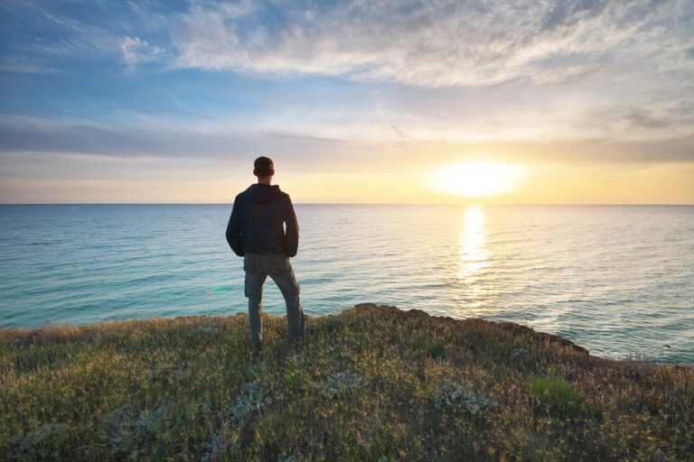 A man stands on a bluff overlooking the ocean.