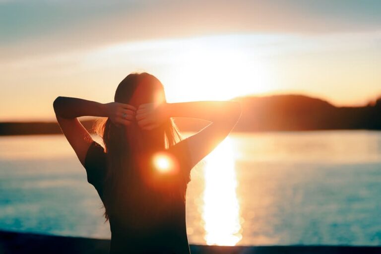 A hopeful woman looking at the sunset by the sea and thinking about alternatives to 12-step recovery.