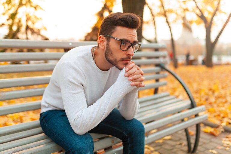 A man sits on a park bench in the fall thinking about getting opioid addiction help.