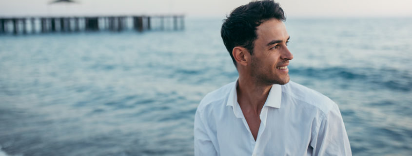 A man smiling by the ocean thinking about his healthy New Year's resolution ideas.