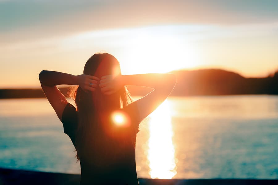 A woman stares at the sun setting over a body of water