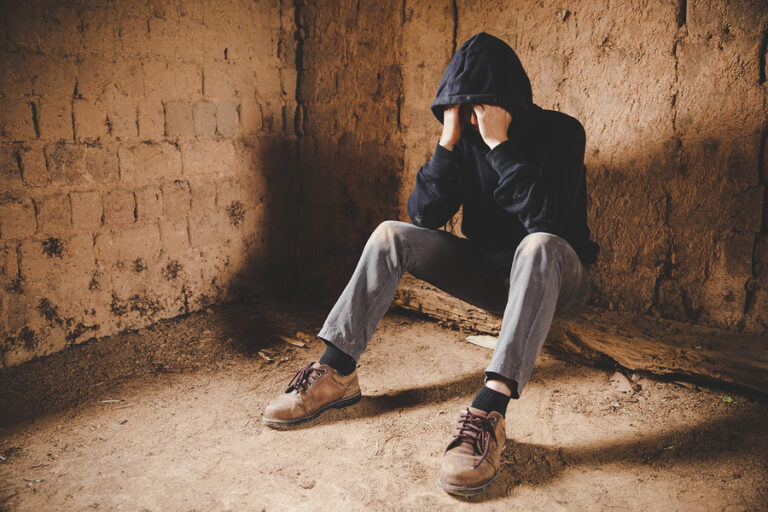 A man sits on the ground and holds his head in his hands