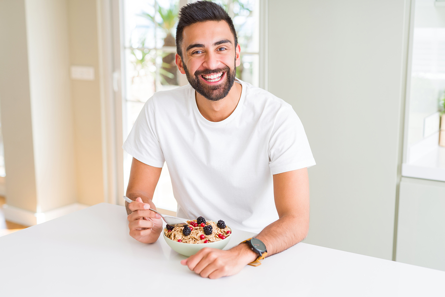 A man smiles while eating a bowl of cereal