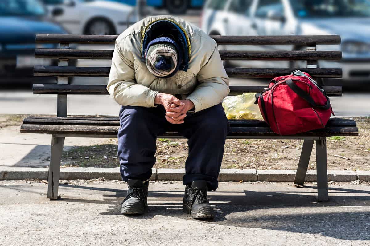 A homeless man sits with his head down on a bench