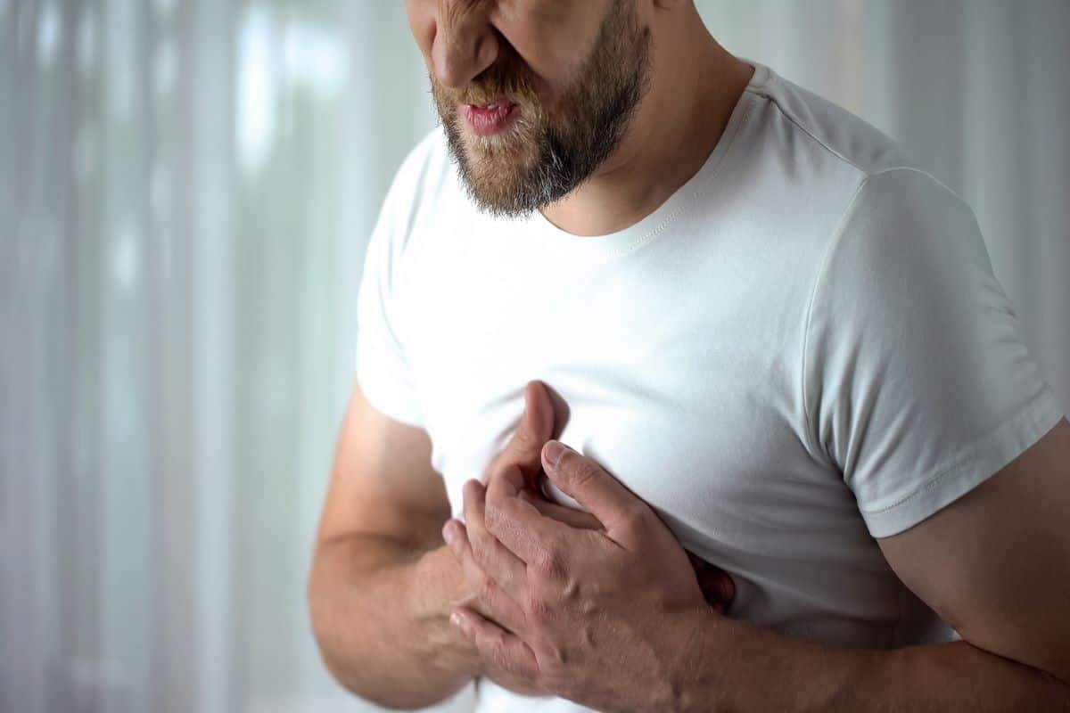 A man grips his chest over his heart in pain due to meth effects on the heart