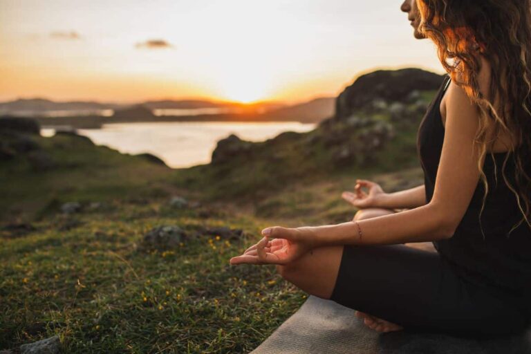 A woman practicing yoga outside with a sunset in the background.
