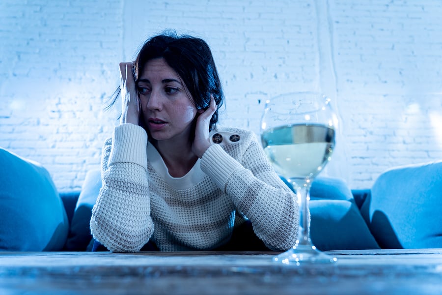 A depressed woman sits with a glass of wine in front of her.