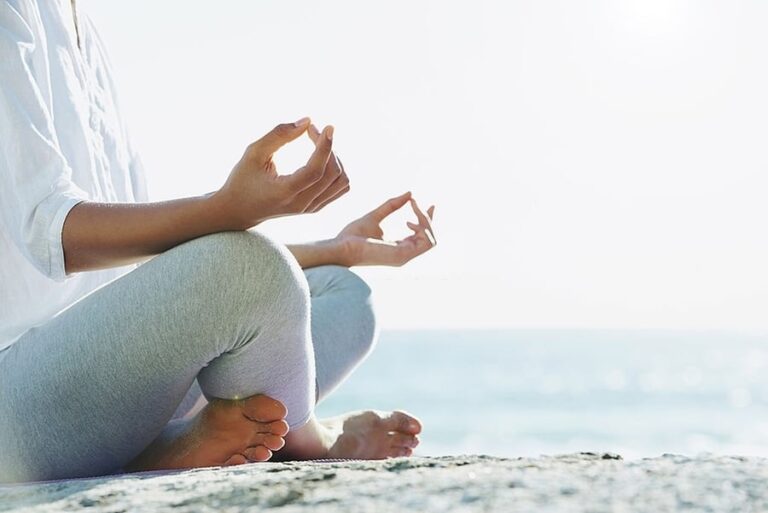 A woman sits and meditates by the ocean.