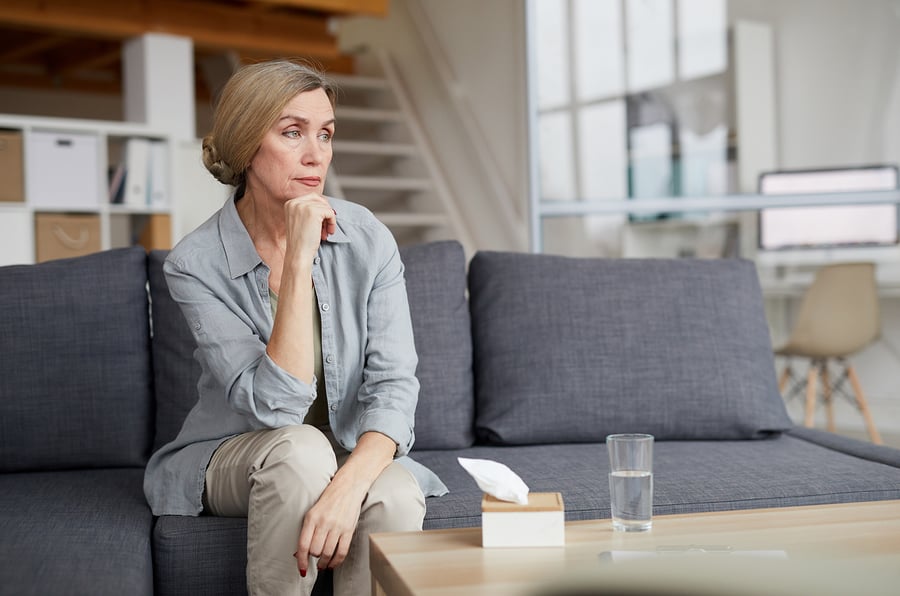 A woman sits on the couch wondering if she should go to rehab during COVID-19.