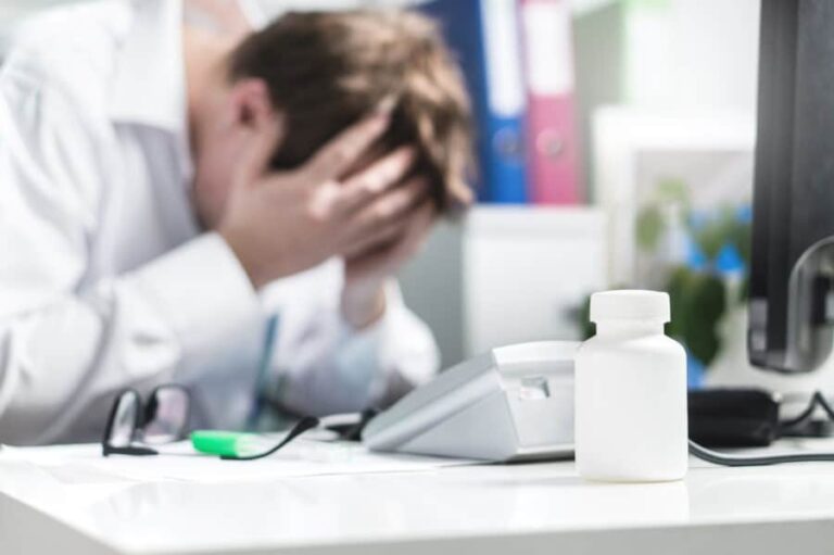 A doctor buries his head in his hands as he deals with stress and addiction.