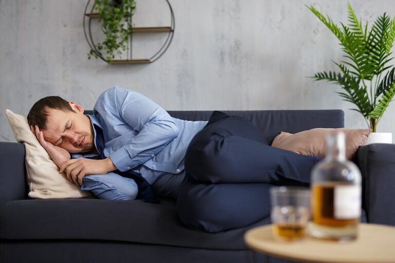 A drunk businessman sleeping on the sofa and suffering from the effects of alcohol abuse.