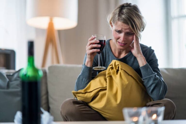 A woman sits on the couch dealing with anxiety after drinking.