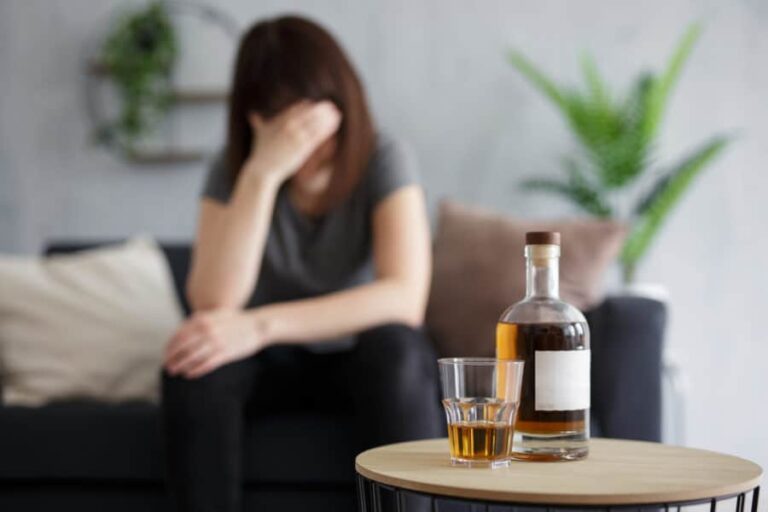 A woman sitting with her head in her hand with alcohol on the table in front of her.