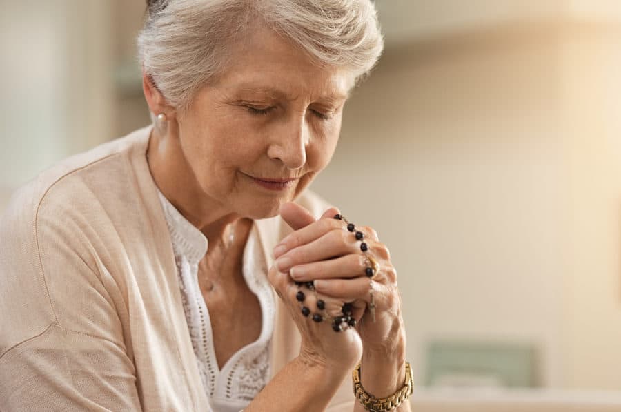 A senior woman practices her spiritual wellness by praying with a rosary.