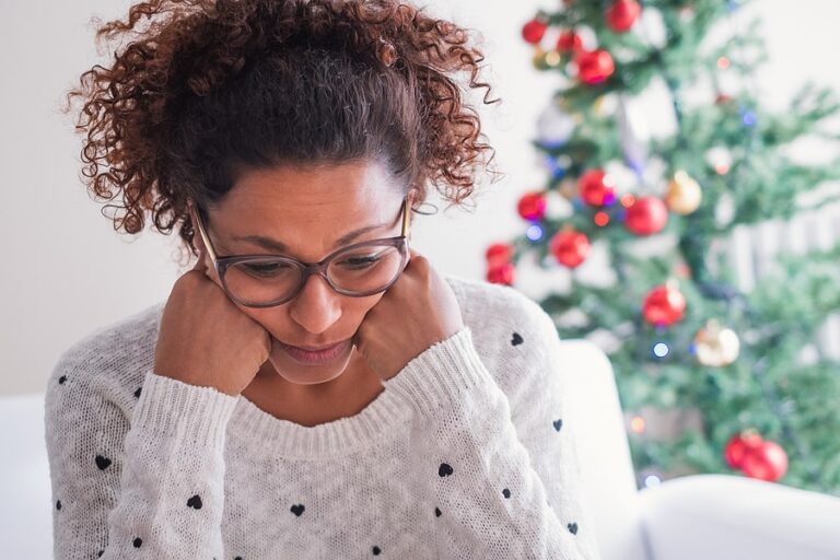 A woman sitting by a Christmas tree, struggling with holiday stress.