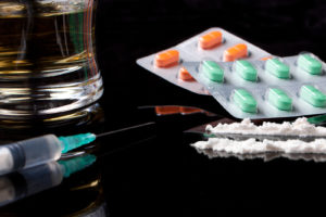 Drugs, pills and alcohol sitting on a dark-surfaced table.