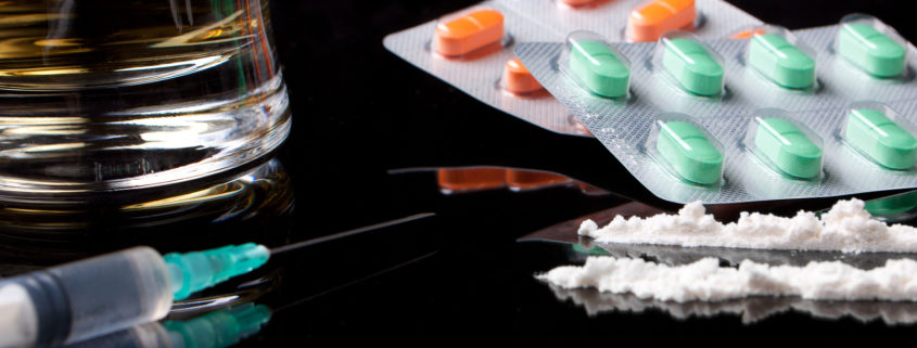 Drugs, pills and alcohol sitting on a dark-surfaced table.