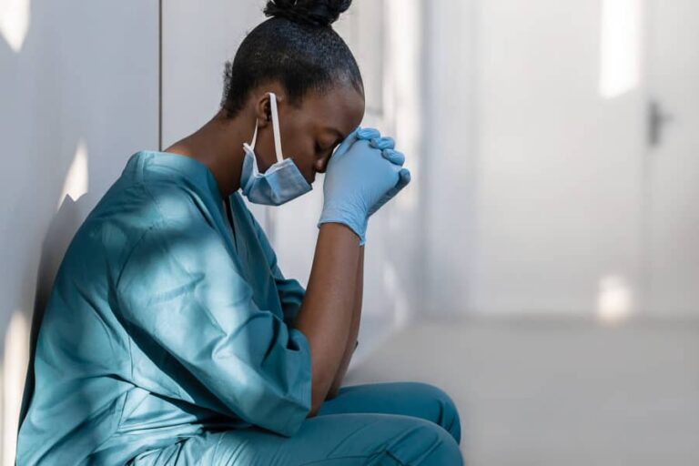 A female nurse hangs her head against her clasped hands, showing the strained mental health of healthcare workers.