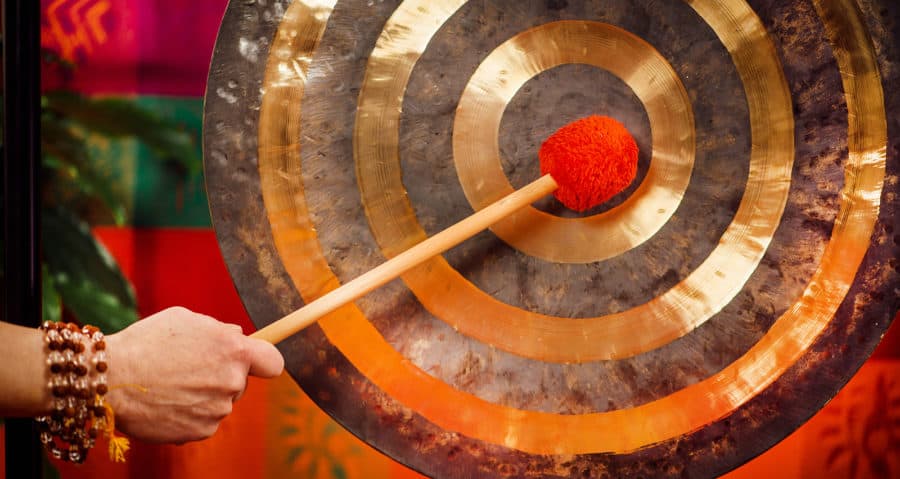 A close-up image of a hand using a mallet to hit a gong in sound therapy for addiction treatment.