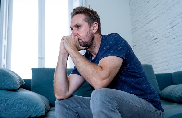 A depressed man sits on his couch and thinks how COVID-19 has impacted his mental health.
