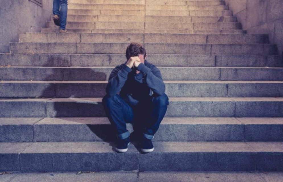 A man who suffers from substance abuse sits on steps outside.