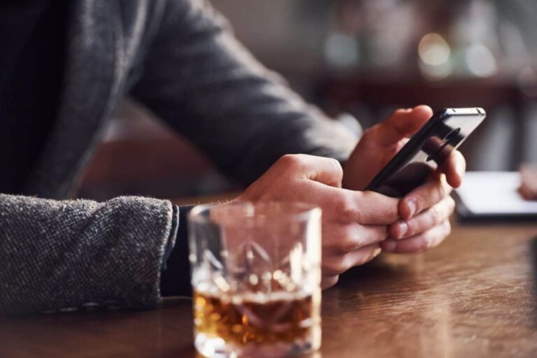 A man with alcohol addiction scrolling through social media while drinking liquor.
