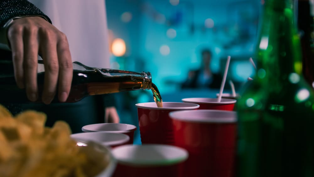 Beer is poured into a red plastic cup at a party.