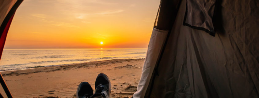 A person sits in a tent to look at the sun rise over the ocean.