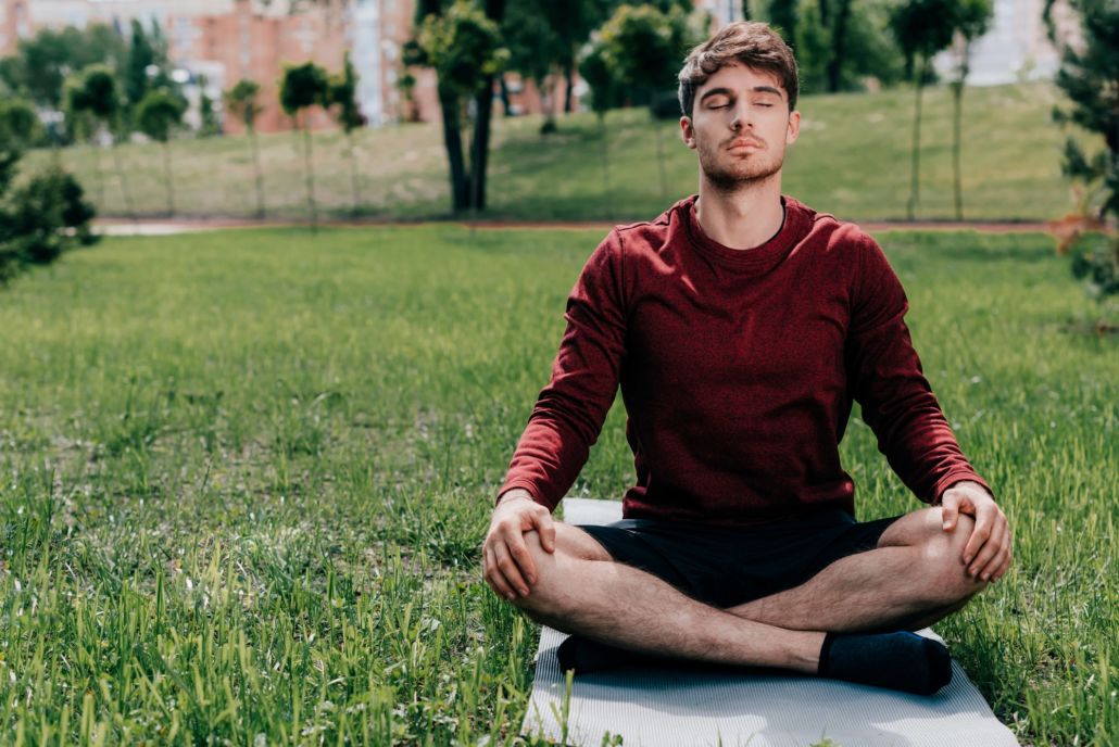 Man doing a yoga pose on a mat with grass background