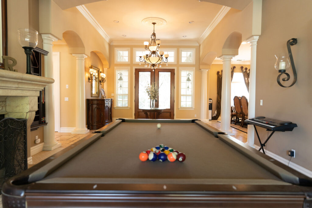 A long interior shot of a pool table leading to the front entrance of a large house