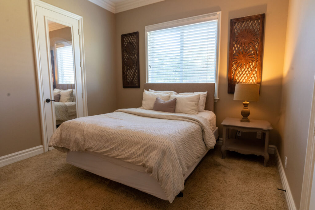 A queen bed under a window with a side table
